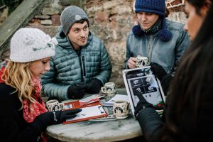 Eine Gruppe steht an einem Glühweinstand auf dem Weihnachtsmarkt in Münster und spielt im Rahmen ihrer Weihnachtsfeier ein Outdoor-Spiel der Adventurebox